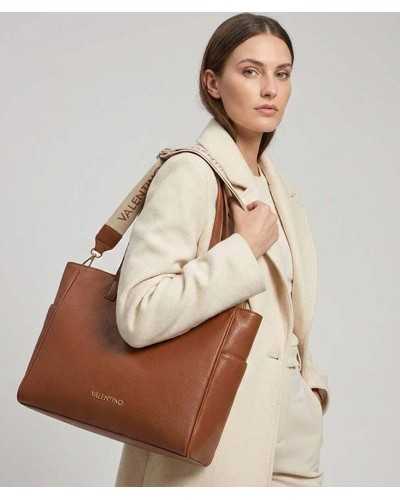 Modelo llevando al hombro bolso tote marrón Valentino Bags con correa logo