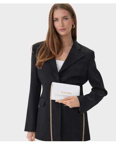 Modelo llevando cartera Valentino Bags blanca con cadena dorada cruzada sobre blazer negro