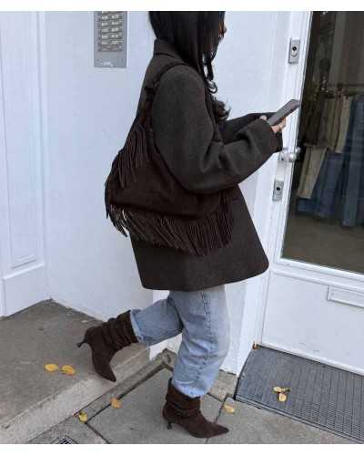 Mujer con botines arrugados marrones, vaqueros claros con bajo vuelto, americana marrón y bolso de ante con flecos