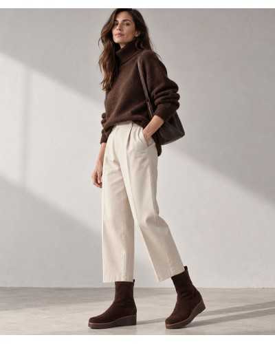 Mujer con botines calcetín marrones, pantalón crudo de pinzas, jersey de cuello alto marrón y bolso marrón