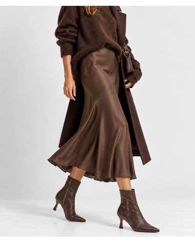 Mujer con botines Dibia chocolate, falda midi satinada, jersey de cuello alto y abrigo marrón