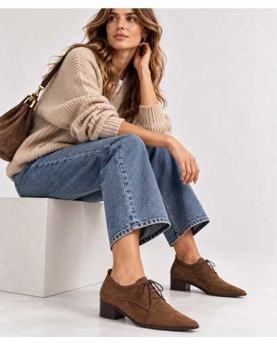Mujer sentada con vaqueros anchos, jersey de punto beige y bluchers color cuero